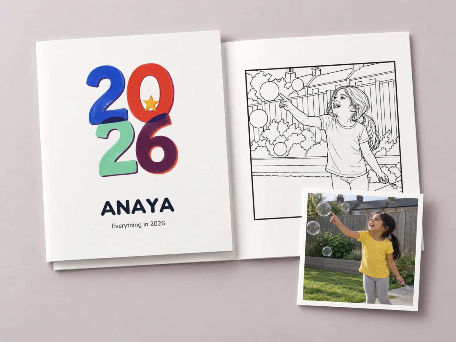 A colouring book with a bold multicoloured 2026 and the name Anaya on its cover, resting on a copy open at a drawing of a laughing girl in her garden reaching out to pop a bubble level with her face, with the photo it came from lying across the corner of the page